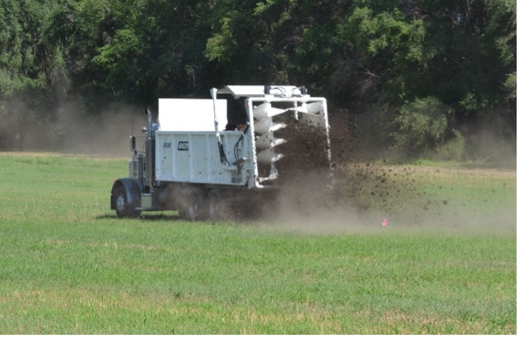 Typical manure spreader broadcasting manure solid to soil as fertilizer amendment.