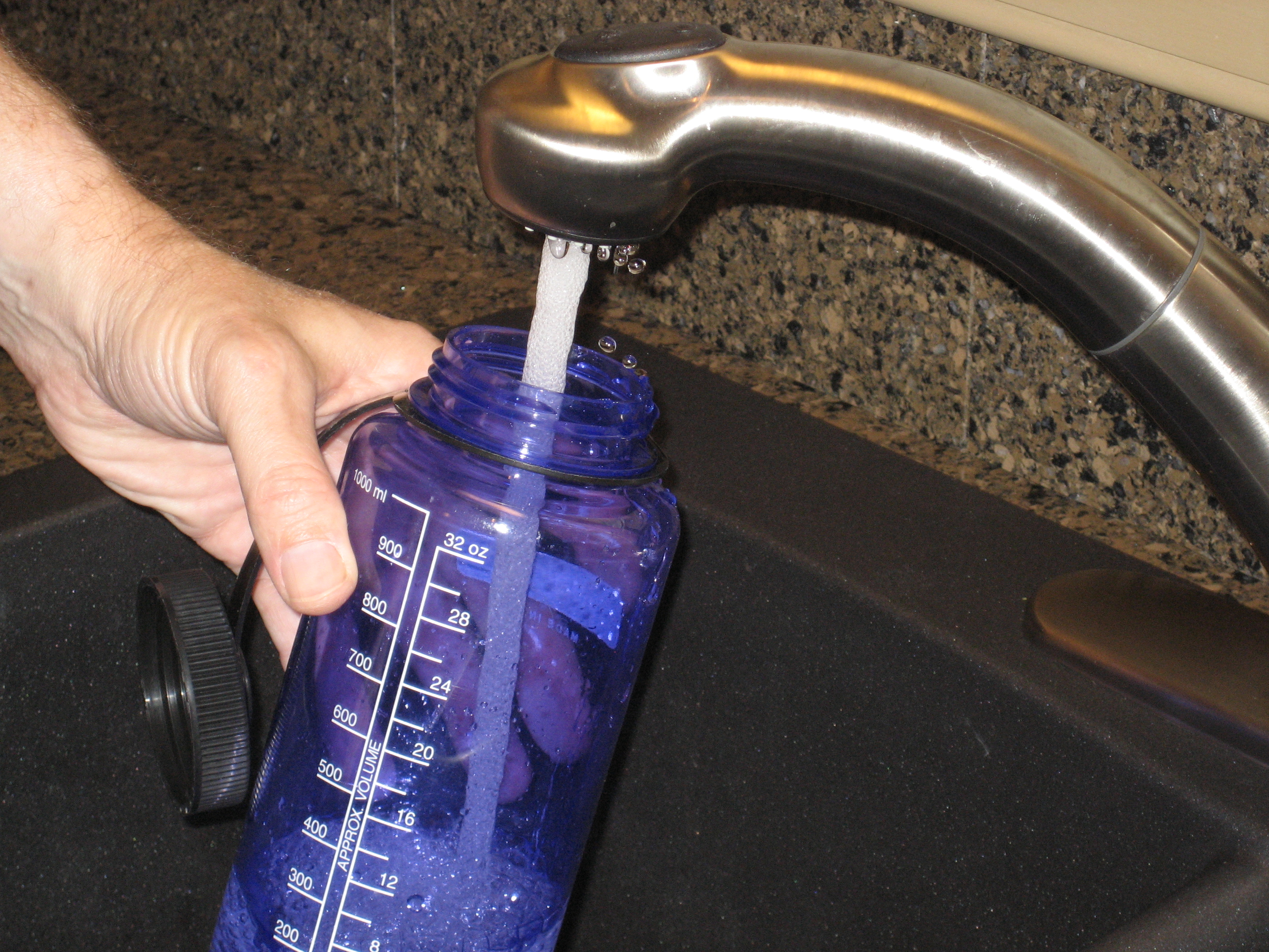 A water bottle being filled at a sink faucet