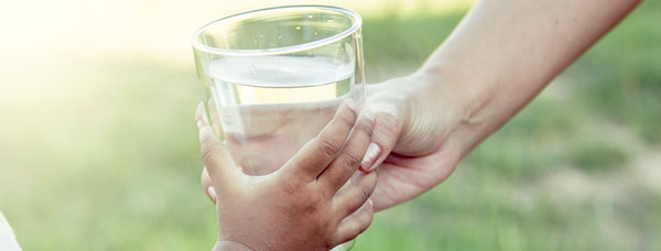 Child and adult holding a glass of water