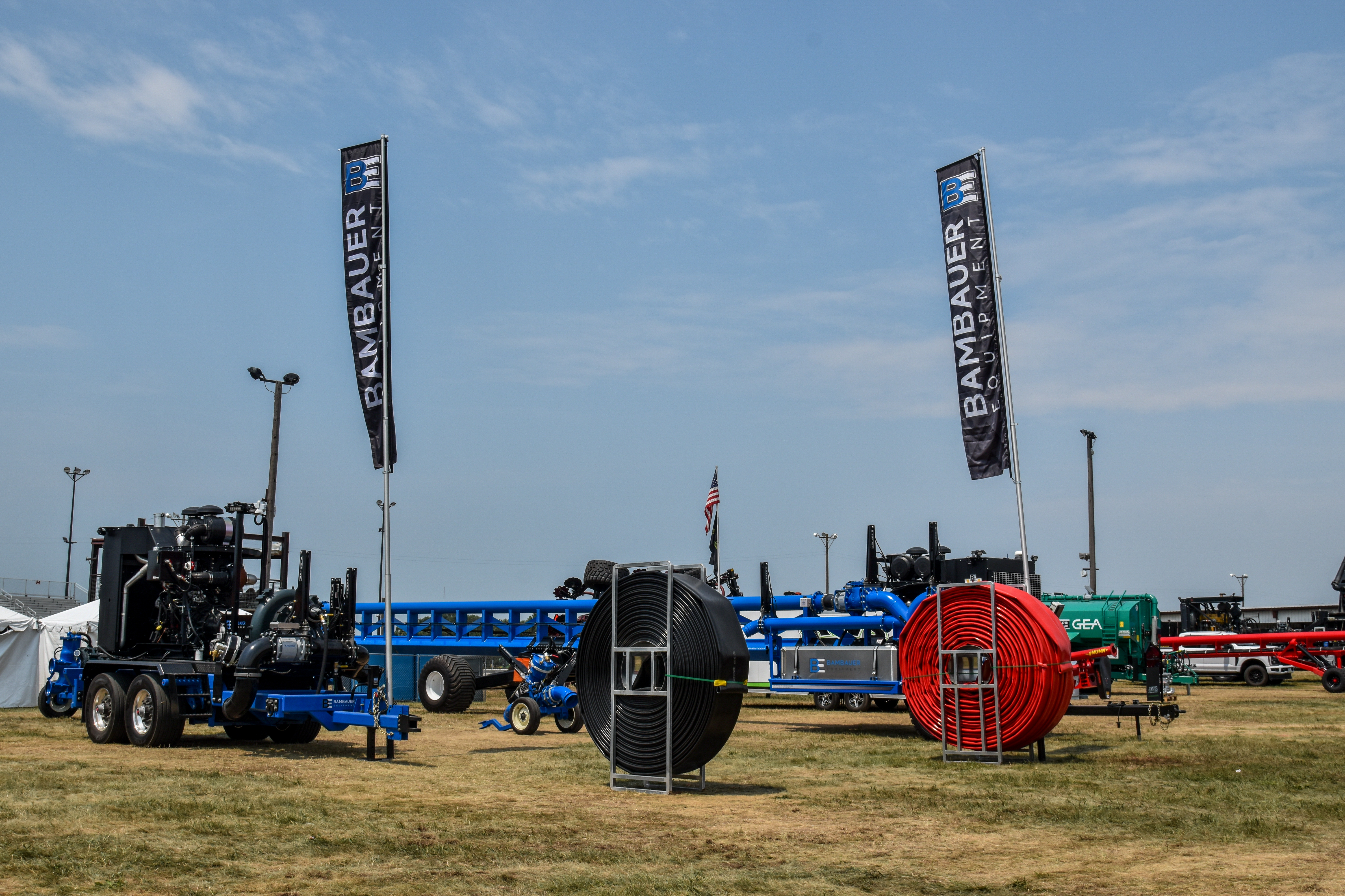 Equipment and machinery displayed outdoors on grass with banners under a clear blue sky.