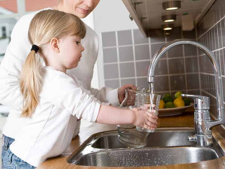 Girl getting a glass of water from a faucet.