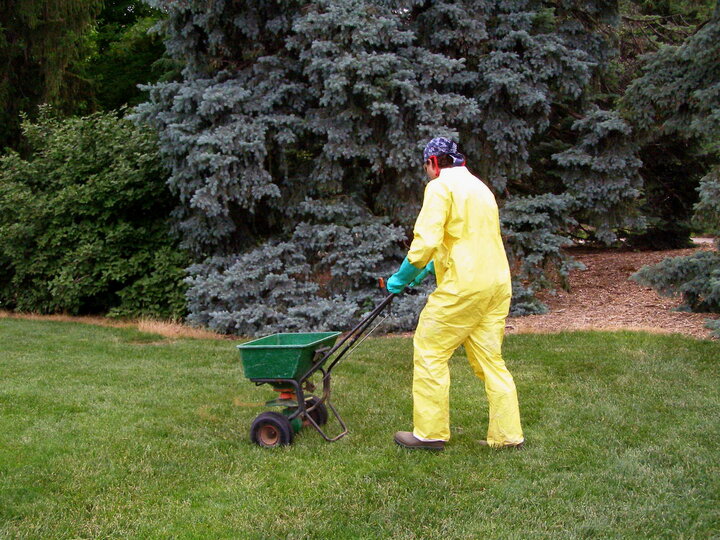 Lawncare professional spreading fertilizer in the correct PPE